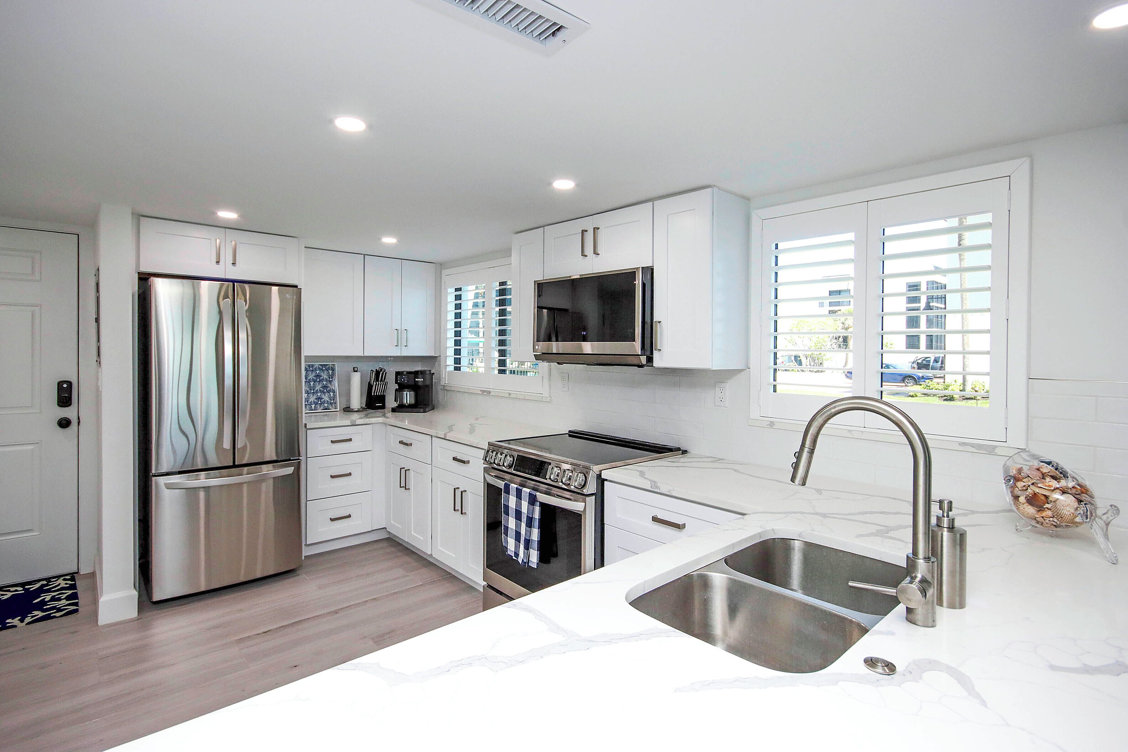 A modern kitchen with stainless steel appliances, white cabinetry, and a large window providing natural light.
