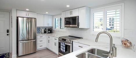 A modern kitchen with stainless steel appliances, white cabinetry, and a large window providing natural light.