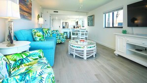 Una sala de estar moderna con un sofá azul, una mesa de centro redonda y un mueble de entretenimiento blanco.