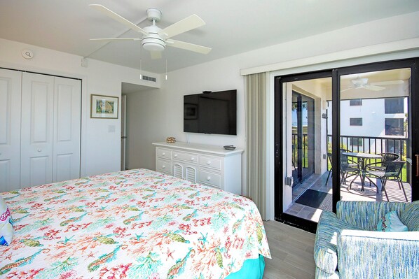 A bedroom with a bed, a dresser, a TV, and a balcony with outdoor furniture. - Beach views - 2nd story condo on Sanibel Island - Sandalfoot 1D2 (Sanibel Island)