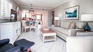 A modern living room with a sofa, coffee table, and chairs. There is a dining area with a table and chairs in the background.