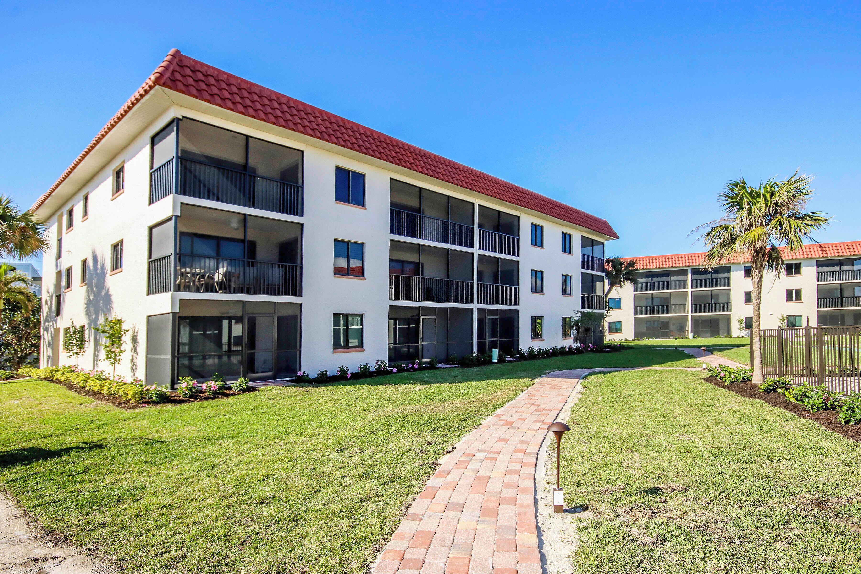A multi-story residential building with a red-tiled roof, balconies, and a paved walkway leading to the entrance.