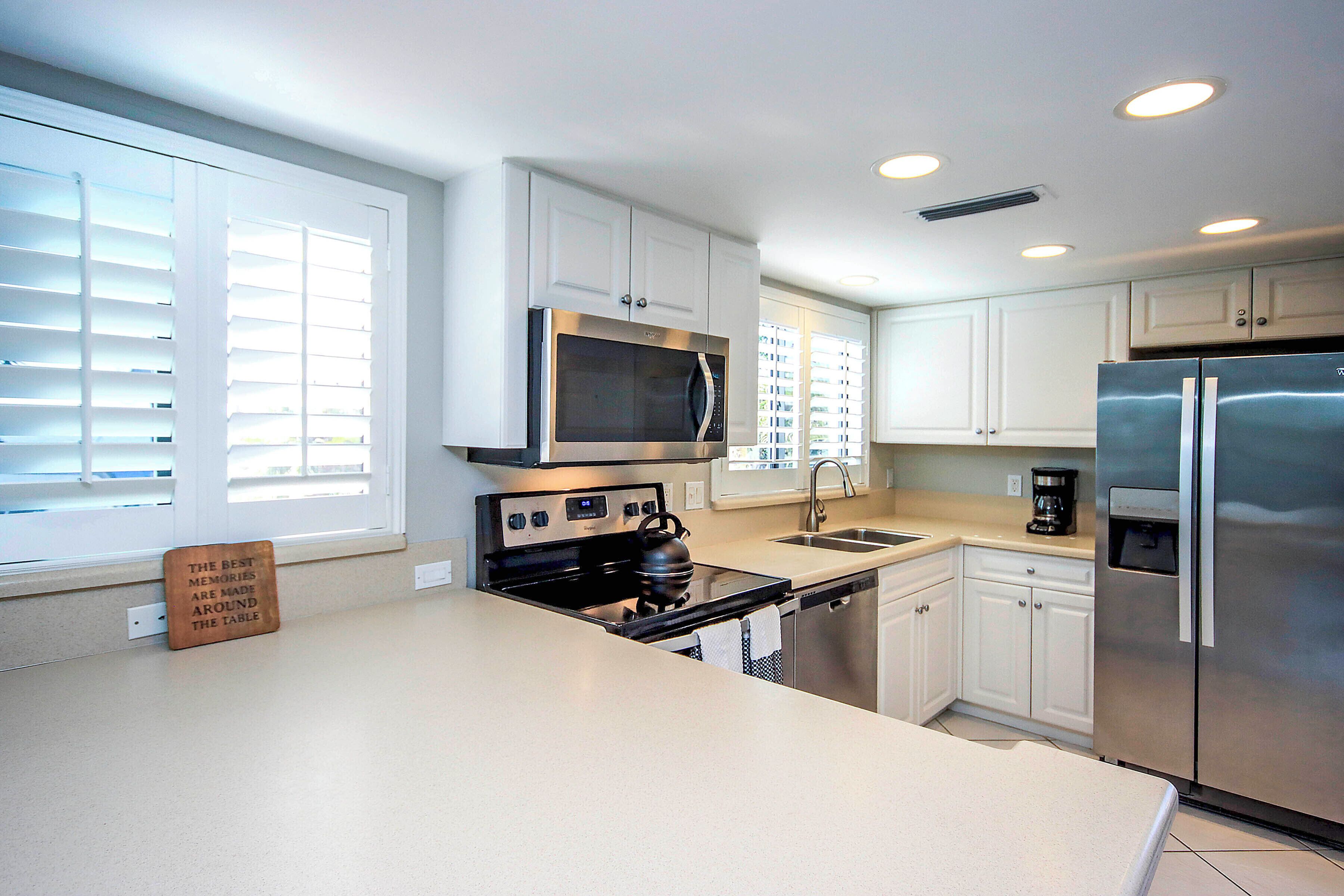 A modern kitchen with white cabinets, stainless steel appliances, and a window with blinds.