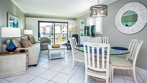 A living room with a sofa, coffee table, and chairs around a glass-top dining table.