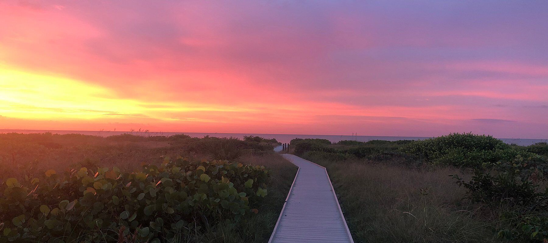A wooden boardwalk leading to a beach with a sunset in the background.