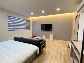 Una habitación de hotel moderna con cama, sofá, televisor y una pequeña mesa.