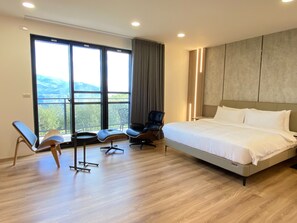 A modern hotel room with a large bed, two chairs, a small table, and a view of the outdoors. - leisurelyinn (Alishan)