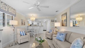 A spacious living room with a beige sofa, a coffee table with a vase of flowers, and a dining area in the background.