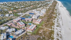 Eine Luftaufnahme einer Küstenregion mit Strand, Wohnhäusern und einem großen Hotelkomplex mit mehreren Gebäuden und einem Schwimmbad.