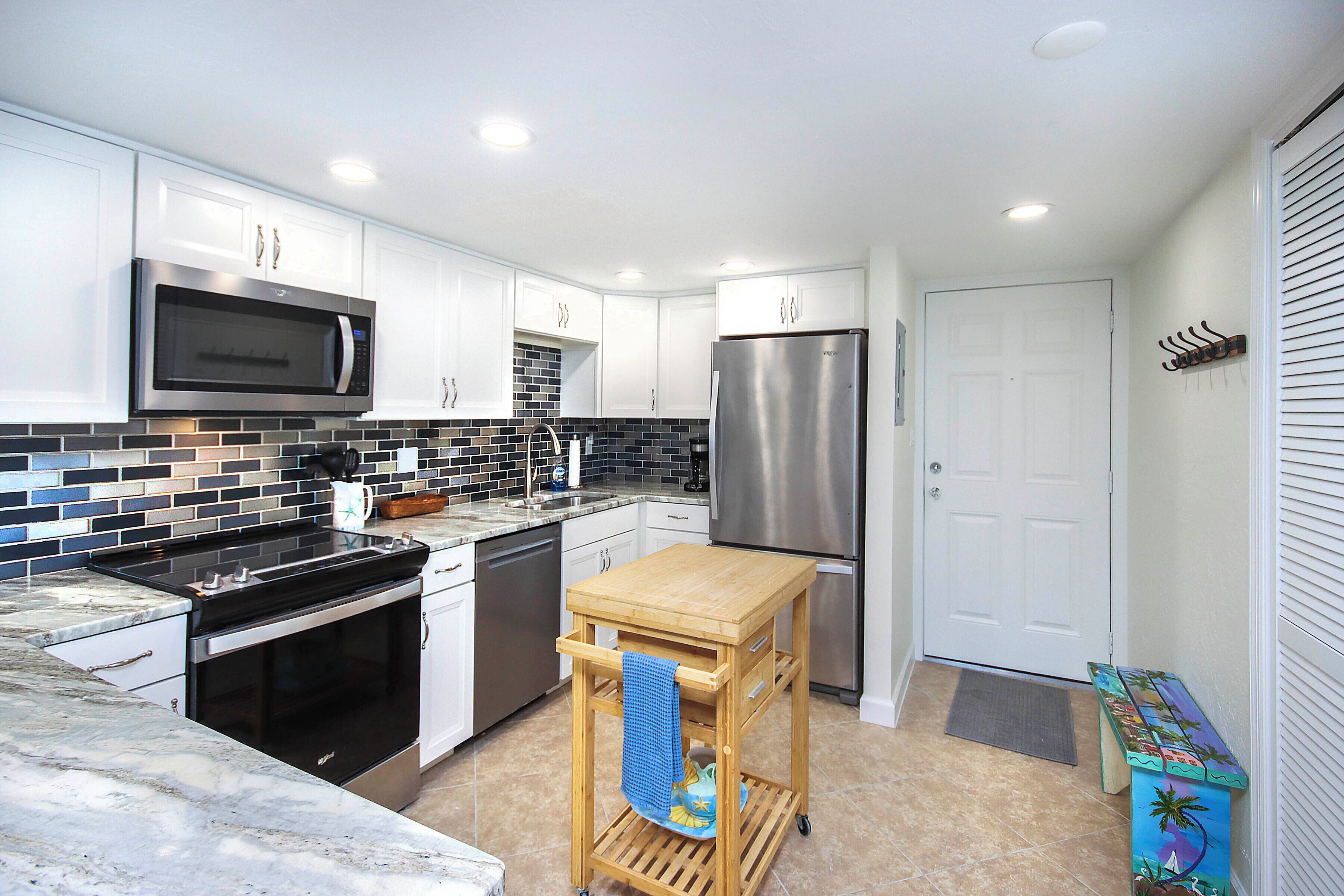 A modern kitchen with white cabinets, a stainless steel microwave, a refrigerator, and a wooden cart with a towel.