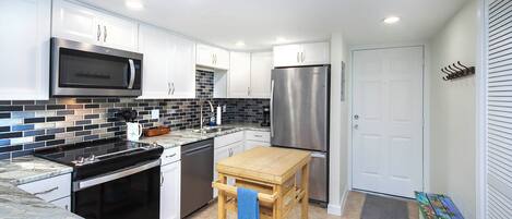 A modern kitchen with white cabinets, a stainless steel microwave, a refrigerator, and a wooden cart with a towel.