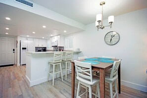 Una cocina moderna con armarios blancos, una mesa de comedor de madera con sillas blancas y un reloj de pared.