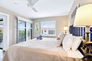 Un dormitorio con cama, ventilador de techo, ventana con persianas y lámpara.