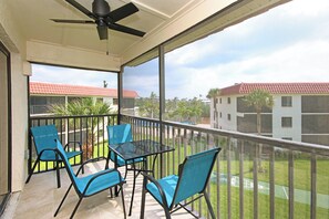 Un balcon avec une table et des chaises, un ventilateur de plafond et une vue sur les bâtiments et la verdure.