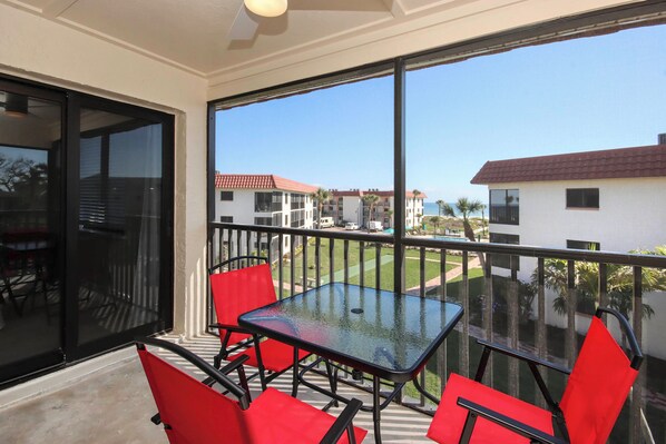 Ein Balkon mit einem Glastisch und roten Stühlen, der auf ein Wohngebiet mit Häusern und Rasenflächen blickt.