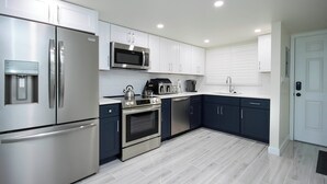 Una cocina moderna con electrodomésticos de acero inoxidable, armarios blancos y suelo de baldosas grises.