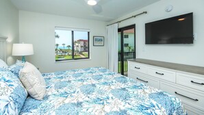 A bedroom with a bed, a ceiling fan, a window with a view, a flat-screen TV, and a dresser.