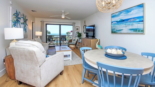 A modern living room with a sofa, coffee table, and dining table with chairs. There is a TV and a painting on the wall. - 3rd Story Sanibel Condo With Coastline Views - Sandalfoot 3C3 (Sanibel Island)