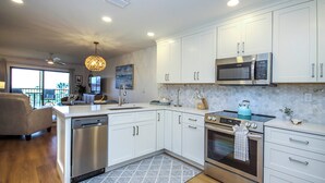 A modern kitchen with white cabinets, stainless steel appliances, and a large island. - 3rd Story Sanibel Condo With Coastline Views - Sandalfoot 3C3 (Sanibel Island)