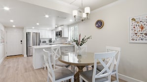 Una cocina moderna con armarios blancos, una isla central y una zona de comedor con una mesa redonda y sillas blancas.