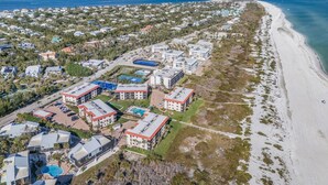 Vista aérea de una zona costera con playa, edificios residenciales y un complejo hotelero grande con varias construcciones y una piscina.