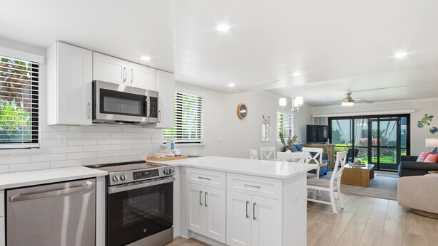 Una cocina moderna con armarios blancos, electrodomésticos de acero inoxidable y un comedor con mesa y sillas blancas.