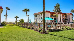 A hotel with a pool area, palm trees, and a fenced courtyard.