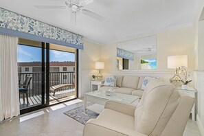 Un salon avec un canapé, une table basse en verre et un balcon agrémenté de meubles en osier.