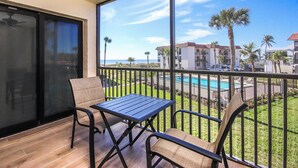 A balcony with a table and chairs, overlooking a pool and palm trees.