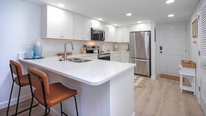 A modern kitchen with white cabinetry, stainless steel appliances, and a central island with bar stools.