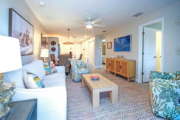 A living room with a white sofa, patterned armchairs, a wooden coffee table, and a ceiling fan. - 3rd floor Sanibel condo with enchanting beach views - Sandalfoot 4C3 (Sanibel Island)