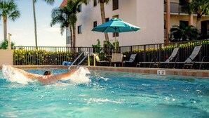 A swimming pool with a person swimming, surrounded by palm trees and a building with a balcony. - Stylish 3rd floor condo on Sanibel Island with ocean views - Sandalfoot 4D3 (Sanibel Island)