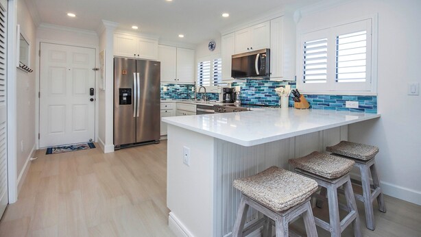 A modern kitchen with white cabinetry, a large island with bar stools, stainless steel appliances, and a blue-tiled backsplash. - Stylish 3rd floor condo on Sanibel Island with ocean views - Sandalfoot 4D3 (Sanibel Island)