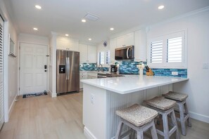 Cocina moderna con muebles blancos, una isla grande con taburetes de bar, electrodomésticos de acero inoxidable y un salpicadero de azulejos azules.