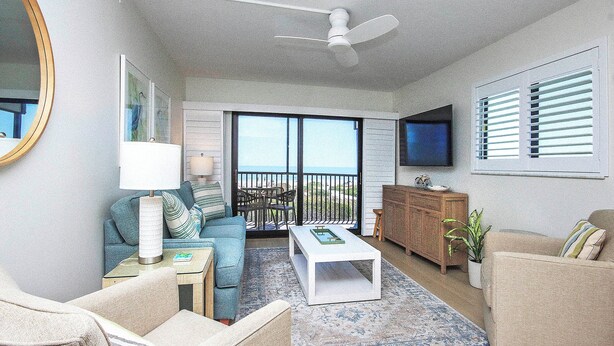 A living room with a sofa, a coffee table, a TV, and a balcony with a view.