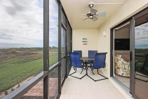 A balcony with a table and chairs, a ceiling fan, and a view of a green landscape.