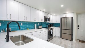 Una cocina moderna con armarios blancos, un lavamanos de acero inoxidable, un microondas, una estufa y un refrigerador.