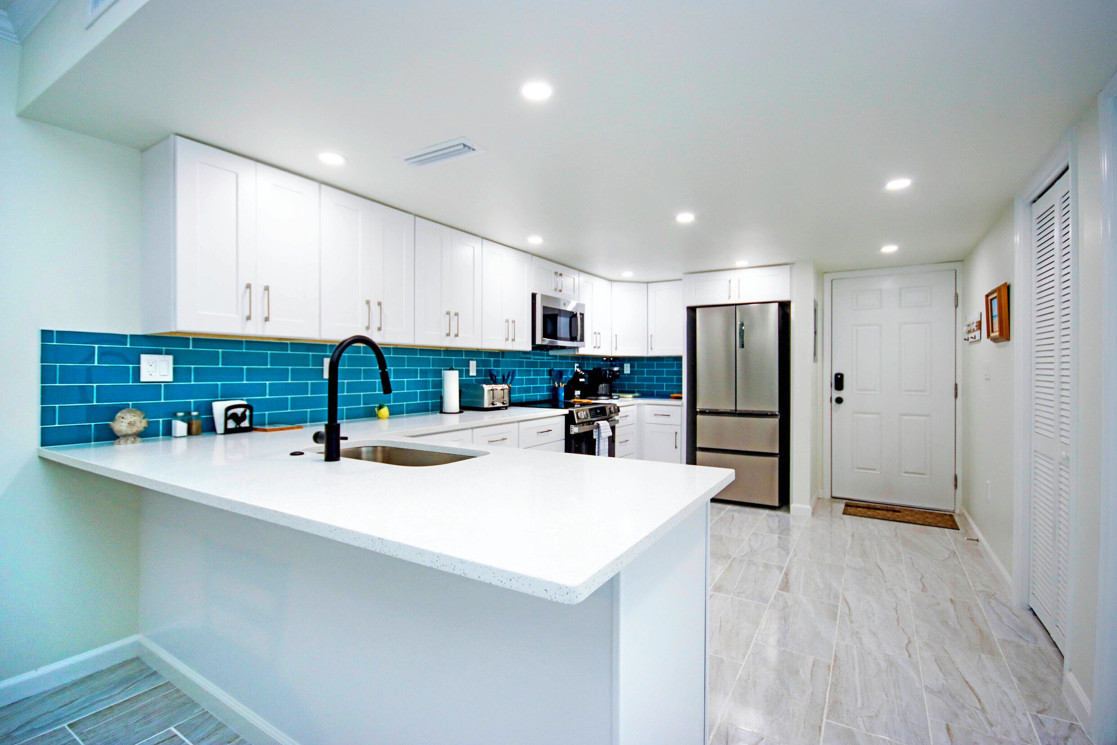 A modern kitchen with white cabinets, a blue backsplash, and stainless steel appliances.