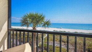 A balcony with a view of a beach and a palm tree. - 3rd Story Sanibel condo with panoramic views of the Gulf - Sandalfoot 5C3 (Sanibel Island)