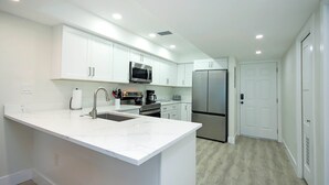 A modern kitchen with white cabinetry, a stainless steel refrigerator, and a marble countertop. - 3rd Story Sanibel condo with panoramic views of the Gulf - Sandalfoot 5C3 (Sanibel Island)