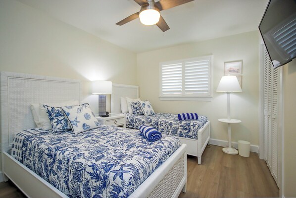 A bedroom with two beds, a ceiling fan, a TV, and a window with blinds.