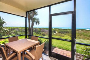 A balcony with a table and chairs, a view of the ocean, and a glass door.