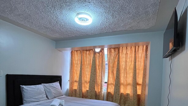 A bedroom with a bed, curtains, a ceiling light, and a TV mounted on the wall. - Hostal El Mariscal  (Urubamba)