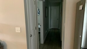Un pasillo estrecho con suelo de madera, una puerta blanca a la izquierda y un refrigerador a la derecha.