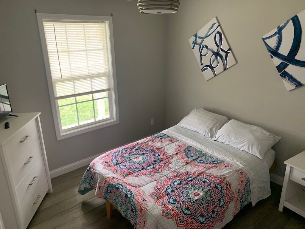 Een slaapkamer met een bed, een raam, een kaptafel en abstracte wanddecoratie.