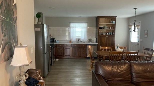 Una cocina moderna con una isla central, armarios de madera y un área de comedor con un sofá de cuero marrón y una lámpara de araña.