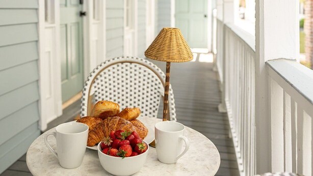 Une véranda abritée avec une table mise pour le petit-déjeuner, comprenant des croissants, des fraises et une tasse.