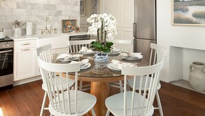 Une cuisine moderne avec des meubles blancs, une table de salle à manger ronde entourée de chaises blanches, un réfrigérateur en acier inoxydable et un pare-feu en pierre.