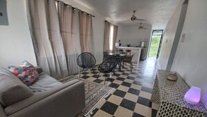 A living area with a sofa, a patterned rug, checkered flooring, a dining table with chairs, and a kitchen area in the background. - Casa Camino Buyé, 6 bedrooms, Private Pool (Cabo Rojo)