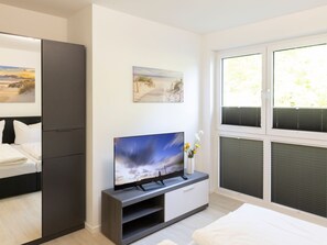 Ett modernt sovrum med en säng, en tv på ett tv-bord, en tavla och ett fönster med persienner.